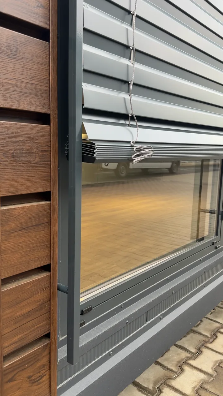 Außenliegende Raffstoren mit Aluminium-Lamellen an einem Modulhaus-Fenster mit Holzfassade